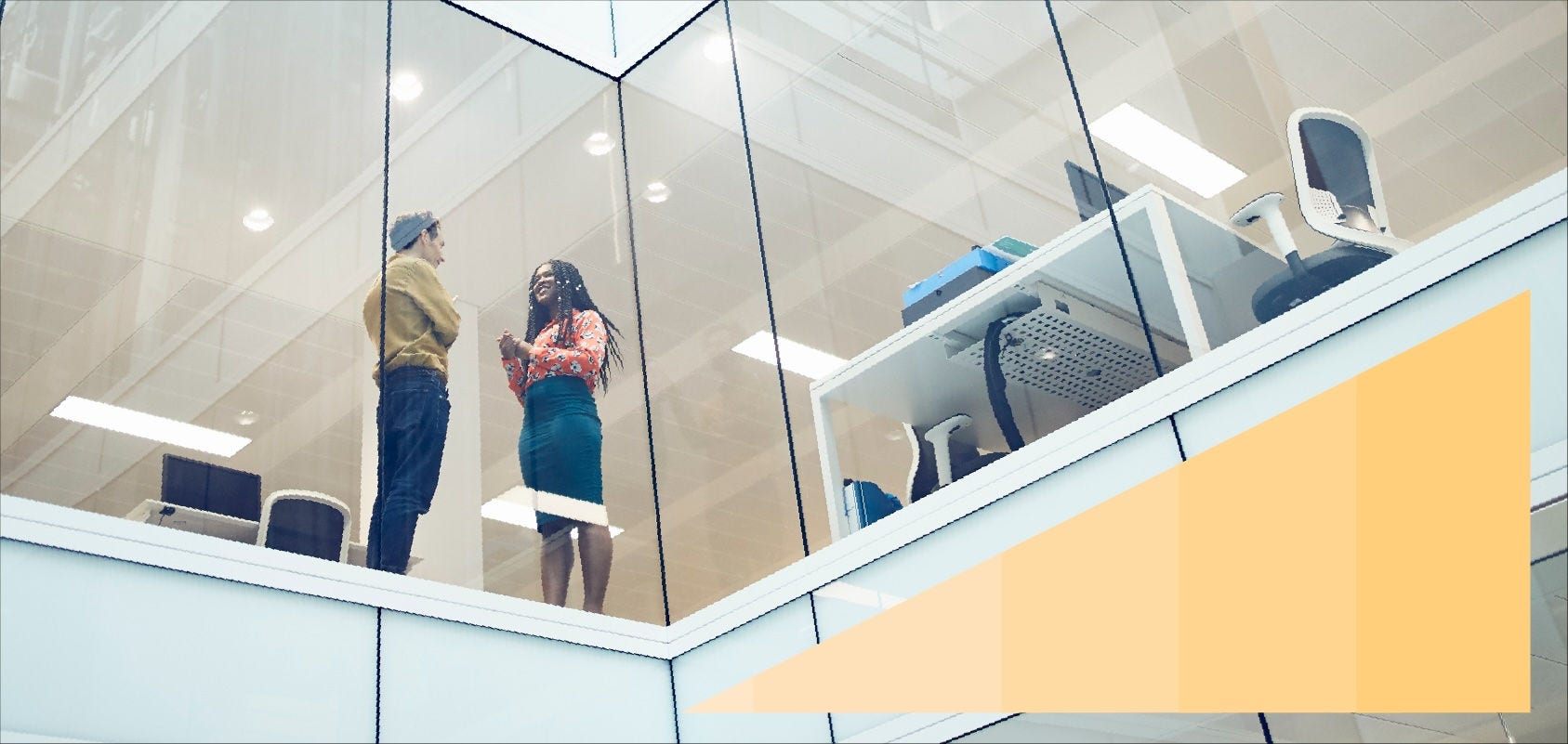 Low-angle photo of two colleagues talking in their office through a glass wall. 